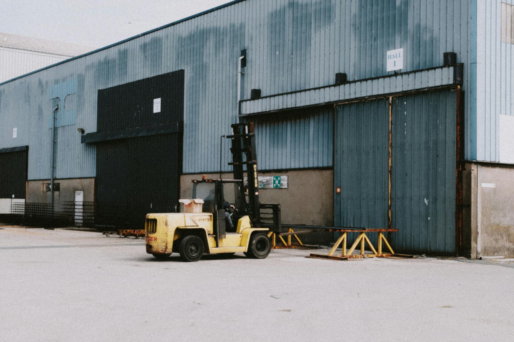 A forklift parked outside an industrial warehouse loading area on a sunny day.