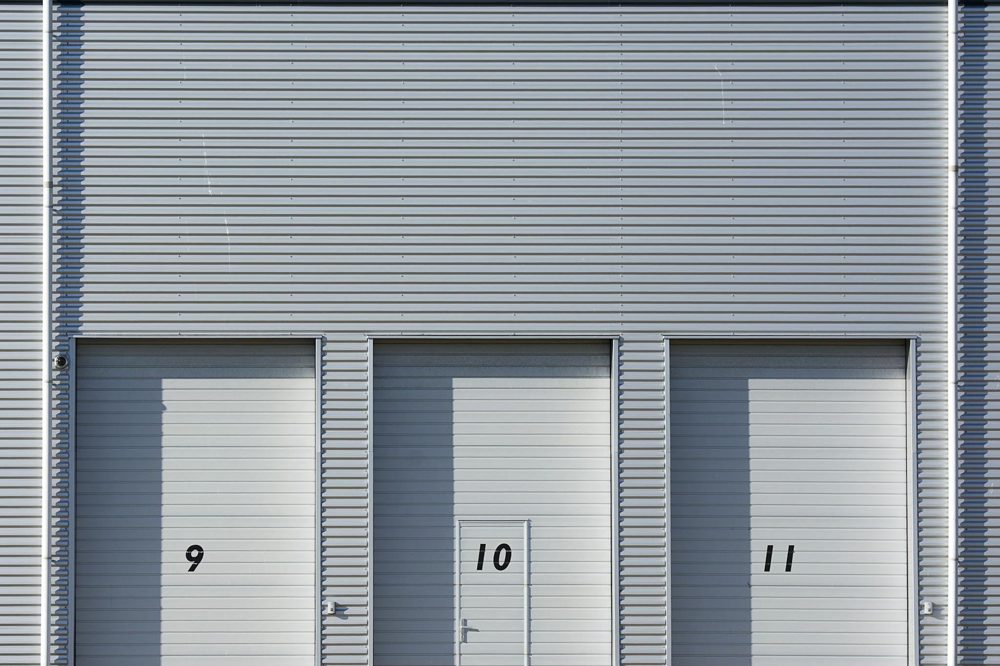 Close-up view of a modern industrial building with metal shutters numbered 9, 10, and 11, showcasing minimalist architecture.